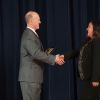 Doctor Potteiger shaking hands with an award recipient in a black blazer and black patterned top